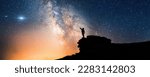 Small photo of Lone person standing on top of rock, pointing with hand towards the Milky Way and the vast expanse of universe. Stunning silhouette of man gazing out into the cosmos. Power of dreams and aspirations.