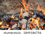 Small photo of A close up on clay pots and jugs being hardened in fire with flaming hot pieces of wood and coal scattered everywhere inside a sandy pit seen during a medieval themed fair in Poland