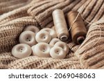 Buttons and a spool of thread with a sewing needle on a beige knitted sweater. Sewing accessories. Copy space.
