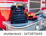 Ballistic vest and red firefighter helmet on fire truck bumper. Concept of evolving role of fire department response to mass casualty shooting and terrorism