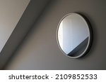 Small photo of Round wall mirror reflections in a light grey room with angled dormer cornice. Sylish elegant and sophisticated. Simple enigmatic monochrome minimalist abstract interior design element.