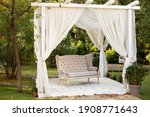 Small photo of Gazebo for relax outdoor. In garden there is podium on which sofa in style of Provence or rustic. Summer gazebo with flowing white curtains. Wedding decorations. Romantic alcove. Decor outdoor terrace