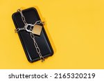 Phone security concept. Smartphone locked with chain and padlock on yellow background. Mobile security and data privacy. Copy space