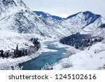 Winter mountain breathtaking landscape, turquoise river running between the mountain slopes, white snow, spruce forest on the banks of the river and mountain peaks, a beautiful impressive view