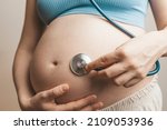 Small photo of Pregnant woman listens to the baby heartbeat and movements with a stethoscope or fetoscope or Pinard Horn. Prenatal fetal health, anxiety, fear concept