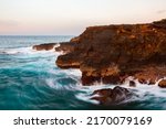 Small photo of A long exposure of turgid blue waves swirling around a rocky Hawaiian coastline