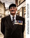 Small photo of Devizes, Wiltshire, UK Oct 2018. Ex-Soldier standing proud with medals and regiment cap in black coat on street for remembrance day poppy appeal.