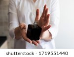 Small photo of Female hands holding black perfume bottle with silver spray cap. Small dicey, cubical form of a bottle. Metal details.