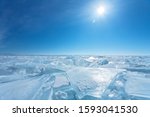 Bright winter sun over a field of ice hummocks with transparent pieces of blue ice. The magnificent landscape of the frozen Baikal Lake. Cold winter background