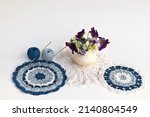 Spring needlework. Still life with beautiful hand crocheted lace napkins, balls of cotton yarn, crochet hooks and a vase with pansies flowers on white background. Crochet as a hobby. DIY concept  