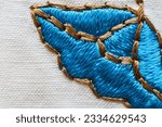 Small photo of Close-up of satin stitch embroidery of floral ornament on a cotton white tablecloth. A bright blue embroidered flower is framed with beige threads. Needlework, DIY concept. Top view, macro, flat lay