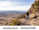 Woman Hikes Along Shelf High Above Desert Road Below in Guadalupe Mountains National Park