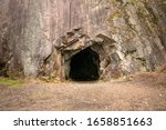 Rock wall with a dark hole, entrance to the cave in Spro, Mineral historic mine. Nesodden Norway. Nesoddtangen peninsula.