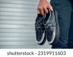 These black creepers with two tone black and white webbing made of leather and with a black flat sole, these elegant and luxurious sneakers are held by a man with a rolling door background
