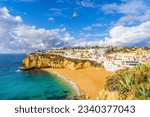 Wide sandy beach, white houses, cloudy sky with seagulls, Carvoeiro, Algarve, Portugal
