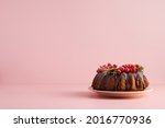 Christmas cake at pink background. Horizontal copy space for text. Cake with chocolate glaze and red currant berries