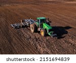 Small photo of John Deere Tractor with cultivator plowing field. Tractor disk harrow on ploughing a soil. Planting in farmland. Sowing seed on plowed field. Farm Machinery cultivating. Russia, Smolensk, 04.26.2022.