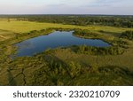 Small photo of Pond in countryside, aerial view. Small lake in agricultural field near forest. Rural landscape. Wet, wild Pond with clean water. Wildlife Refuge Wetland Restoration, groundwater. Green Nature.
