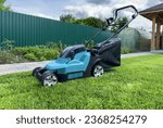 Small photo of Lawn Mower Electric for cutting grass in garden. Сutting grass in yard using Lawn Mower. Lawn mowing machine. Grass Trimmer and Grass Cutter. Lawn maintenance service. Gardener mows weeds