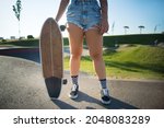 Close-up of young woman holding longboard. Girl in checkered socks and shorts holding skateboard. Sport, hobby, active lifestyle concept