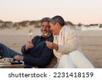 Senior couple enjoying picnic at seashore, holding sparklers and laughing. Lady with short hair and happy grey-haired man having fun together at sunset on the beach. Love, relationship concept