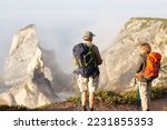 Back view of sporty elderly family hiking on summer. Man and woman in casual clothes and with ammunition looking at mountains. Hobby, active lifestyle concept
