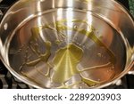 View of a stainless steel frying pan with olive oil heating up on top of a stove.