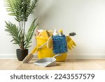 Brushes, bottles with cleaning liquids, sponges, rag and yellow rubber gloves on white background. Cleaning supplies in the yellow bucket on the wooden floor. Cleaning company service advertisement