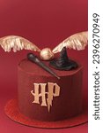Small photo of KYIV, UKRAINE - November 03: Harry Potter cake on the burgundy red background. Birthday magic cake with red velvet chocolate coating decorated with mastic Sorting Hat, Elder Wand and Golden Snitch