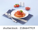 Spaghetti with guanciale or bacon and tomato sauce in white plate on place mat and blue background.