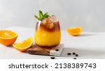 Small photo of Glass of colorful cocktail of bumble or crazy bee with orange juice and espresso coffee on white table with fresh oranges. Trendy summer coffee drink. Menu, recipe. Copy space for text