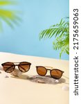 Small photo of Sunglasses sale concept. Trendy sunglasses on beach with green palm leaves. Trendy Fashion summer accessories. Vertical, copy space. Optic store. Vacation, travel concept. Sunglass offer poster