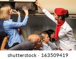 Friendly flight attendant helping passenger to put luggage cabin compartment