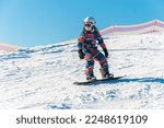 Small photo of Logoisk. Belarus. 01.09.2023. A teenage snowboarder descends the slope of a snow-covered mountain in special equipment. Snowboarding - descent at high speed on a special projectile - a snowboard.