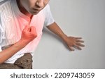 Small photo of Asian young man suffering from central chest pain. Chest pain can be caused by heart attack, myocardial infarct or ischemia, myocarditis, pneumonia, oesophagitis, stress, anxiety, etc,.
