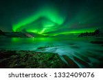 Aurora over Ersfjord and Tugeneset rocky coast with mountains in background, Norway