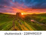 Small photo of Sunset with sun star in Scotland on the Isle of Skye. Landscape with rocks Castle Ewen in summer. yellow orange red sky with clouds. Sandy road to rocks and hills with green grass. Road and small lake