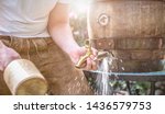 Small photo of Bavarian man in leather trousers stabs a wooden barrel of beer in the garden and enjoys the first sip