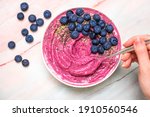 Pink Smoothie Bowl with Blueberries and Hand Using Spoon