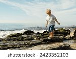 Small photo of little blond boy playing on the seashore. child playing on the seashore. boy stands on stones in the water. child playing on the seashore