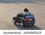 little girl with a tail drives a toy black car on asphalt in a square in the city