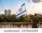 Small photo of A guy in a soldier's uniform with an Israeli flag in his hand against a cloudy sky. Remembrance Day - Yom HaZikaron, Patriotic holiday, Israeli Independence Day - Yom Ha'atzmaut concept.