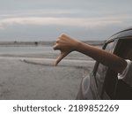Small photo of The hand of a girl standing out of the car with thumbs down. Poor driving and inaccurate route reviews