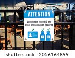 Small photo of Government issued ID and proof of vaccination required sign against blurred restaurant entry and patio seats. Proof of COVID-19 vaccination, two doses fully vaccinated required to access businesses.