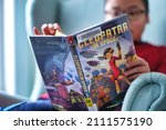Small photo of Toronto, Ontario, Canada - January 22, 2022 : Student boy reading graphic novel book Cleopatra in space borrowed from public library at home.