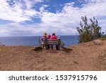 Small photo of A mother and three kids sitting on a bench at a viewpoint at Ohai trail. A family resting on a bench overlooking Pacific ocean after hiking on a trail