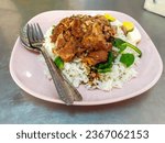Small photo of close up of Stewed pork leg on rice. delicious meal consists of white rice and a stir fry with chicken, onions, red peppers, and greens on pink plate. The strewed has a brown sauce