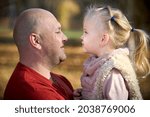 Small photo of Scene of quiet family happiness filiation and love. Happy caucasian father and his little daughter face to face closely looking into each others eyes in sunny autumn park among fallen golden leaves.