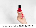 red nail polish bottle in a female hand with red manicure. hand skin care concept. Template for advertising. white background with copy space.