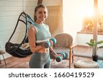 Determined woman losing weight at home and exercising with dumbbells. Sport and recreation concept. Beautiful woman in sportswear with blue dumbbells in her hands.